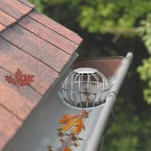 Stainless steel wire basket downspout strainer installed in a residential gutter system, filled with fallen autumn leaves to demonstrate effective clog prevention and leaf protection.