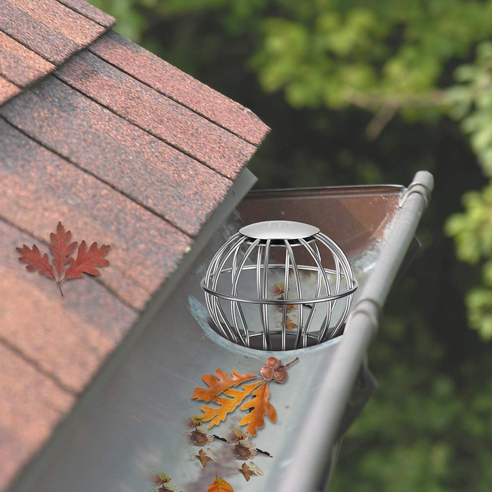 Stainless steel wire basket downspout strainer installed in a residential gutter system, filled with fallen autumn leaves to demonstrate effective clog prevention and leaf protection.