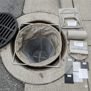 A high-angle, top-down view showing a storm drain filter bag installed inside a circular underground catch basin for stormwater management. Storm Drain Filter Bag